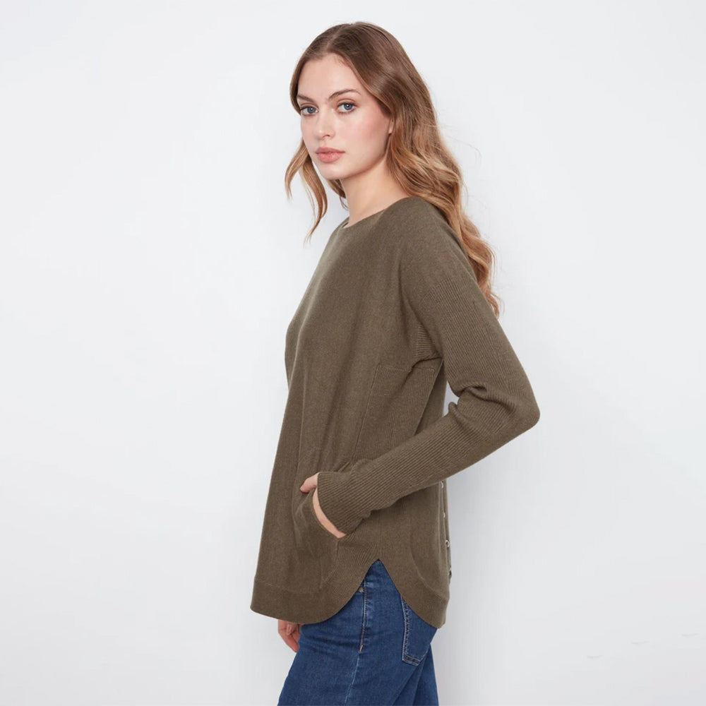 A woman modeling a long-sleeve knit sweater in olive brown, paired with blue jeans, against a plain white studio background.