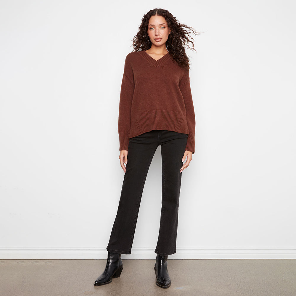 A woman modeling a brown ribbed V-neck sweater and black wide-leg cropped pants with black ankle boots, standing against a white wall.