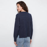A woman wearing a dark navy blue knit sweater and light wash blue jeans, photographed from the back against a plain white studio background.