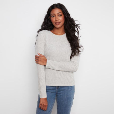 A woman modeling a light gray ribbed knit long-sleeve top with blue jeans, standing against a plain white studio background.