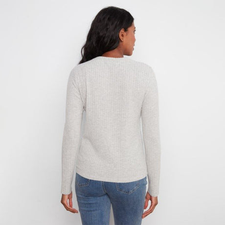 A woman viewed from the back wearing a light beige ribbed knit sweater and blue jeans against a plain white studio background.