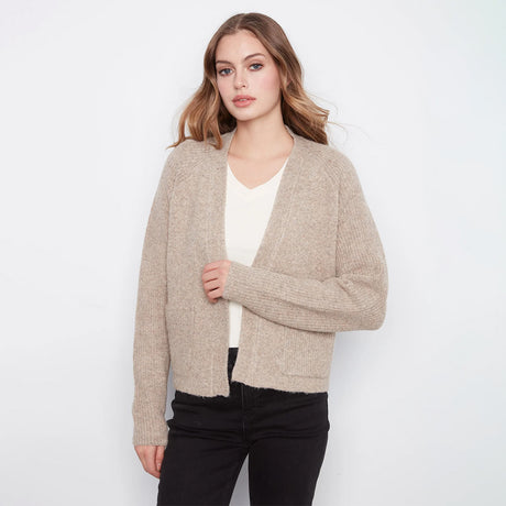 A woman modeling a light beige open-front knit cardigan over a white top and black pants, photographed against a plain light gray studio background.