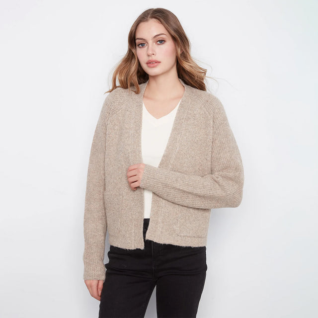 A woman modeling a light beige open-front knit cardigan over a white top and black pants, photographed against a plain light gray studio background.