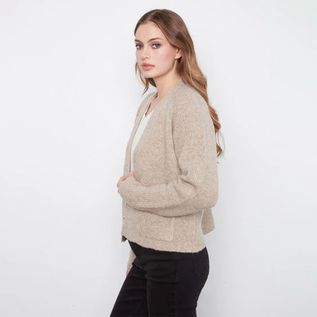 A woman modeling a light beige ribbed knit cardigan over a white top and black pants, standing against a plain white studio background.