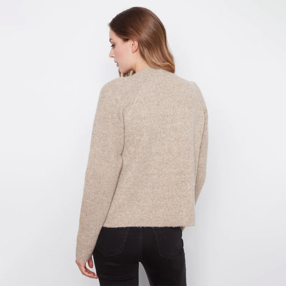 A woman shown from the back wearing a light beige textured knit sweater and black pants against a plain white studio background.
