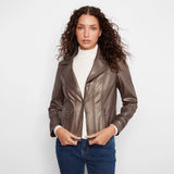 A woman modeling a metallic bronze faux-leather moto jacket over a white ribbed turtleneck and blue jeans, photographed against a clean white studio background.