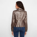 A woman viewed from the back wearing a metallic taupe-brown faux leather jacket and blue jeans, standing against a plain white studio background.