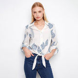 Woman wearing a white blouse with blue floral patterns and blue jeans on a white background