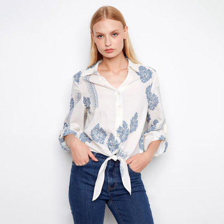 Woman wearing a white blouse with blue floral patterns and blue jeans on a white background