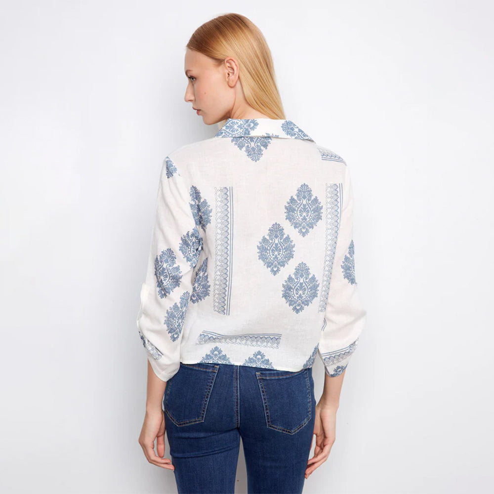 Woman wearing a white blouse with blue floral patterns and blue jeans on a white background