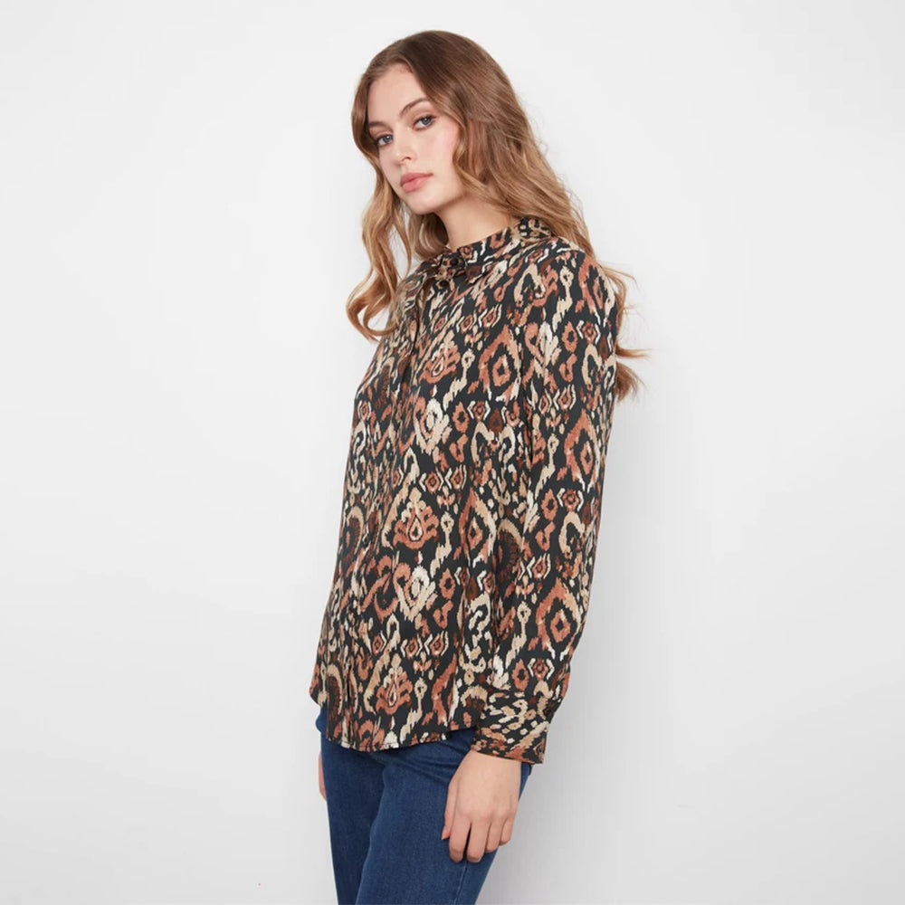 A woman wearing a long-sleeve patterned blouse with an abstract geometric print in brown, beige, and black, paired with blue jeans, photographed against a plain white studio background.
