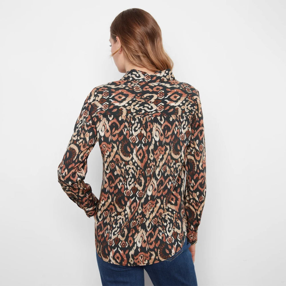 A woman viewed from the back wearing a long-sleeve button-up shirt with an intricate multicolor ikat pattern in brown, beige, and black, paired with blue jeans against a plain white background.