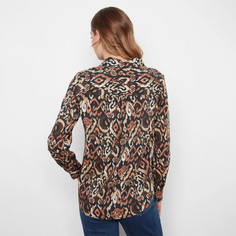 A woman viewed from the back wearing a long-sleeve button-up shirt with an intricate multicolor ikat pattern in brown, beige, and black, paired with blue jeans against a plain white background.