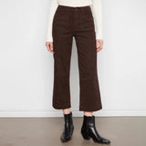 A model wearing dark brown cropped wide-leg trousers with a textured tweed-like pattern, styled with a cream ribbed long-sleeve top and black ankle boots against a white wall and gray floor.