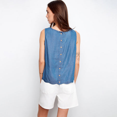Woman wearing a blue sleeveless shirt with buttons and white shorts on a plain background