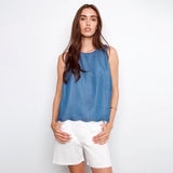 Woman wearing a blue sleeveless top and white shorts on a white background