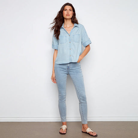 Woman wearing a light blue denim shirt and jeans against a white background