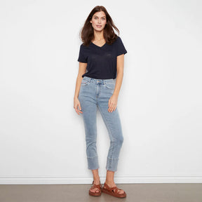 Woman wearing a navy t-shirt and light blue jeans against a white wall.