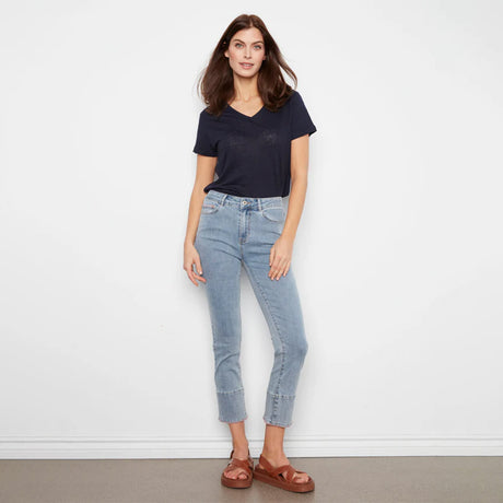 Woman wearing a navy t-shirt and light blue jeans against a white wall.