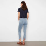 Woman wearing light blue jeans and a dark blue shirt against a white wall.