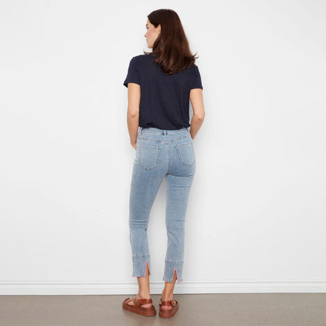 Woman wearing light blue jeans and a dark blue shirt against a white wall.