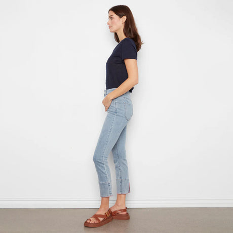 Woman wearing light blue jeans and a navy top against a white wall