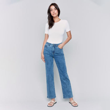 Woman wearing a white top and blue jeans on a gray background