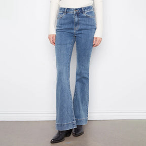 A person wearing medium-wash blue flare jeans with a straight rise and cuffed hems, paired with a cream ribbed long-sleeve top and black ankle boots, standing against a white wall.