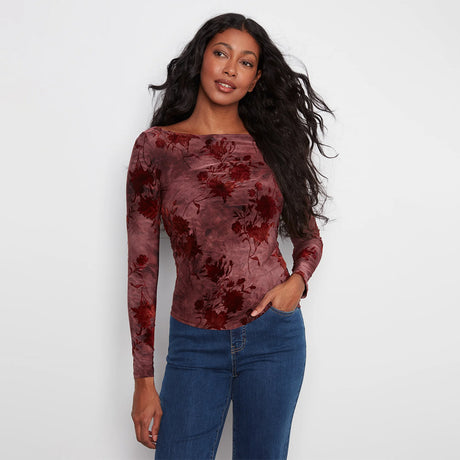 A woman modeling a long-sleeve boat-neck top with a dusty rose and dark red floral jacquard pattern, paired with blue jeans, against a plain white background.