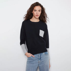 A woman modeling a black knit sweater with light gray contrast panels on the chest and sleeves, paired with light blue jeans, against a plain white studio background.