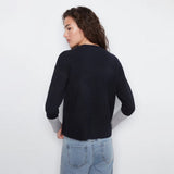 A woman shown from the back wearing a dark navy knit sweater with light gray ribbed cuffs, paired with light blue jeans, against a plain white background.