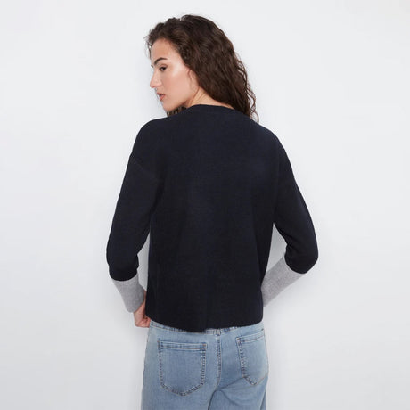 A woman shown from the back wearing a dark navy knit sweater with light gray ribbed cuffs, paired with light blue jeans, against a plain white background.