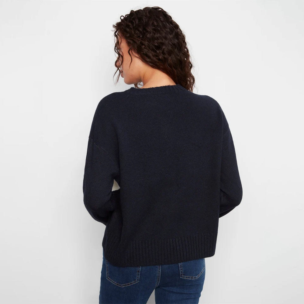A woman viewed from behind wearing a dark navy blue knit sweater and blue jeans against a plain white background.