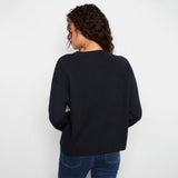 A woman viewed from behind wearing a dark navy blue knit sweater and blue jeans against a plain white background.