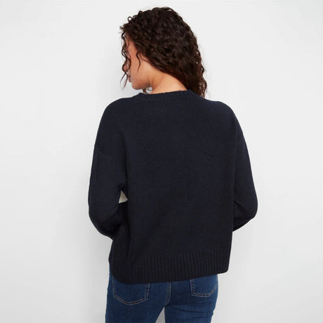 A woman viewed from behind wearing a dark navy blue knit sweater and blue jeans against a plain white background.