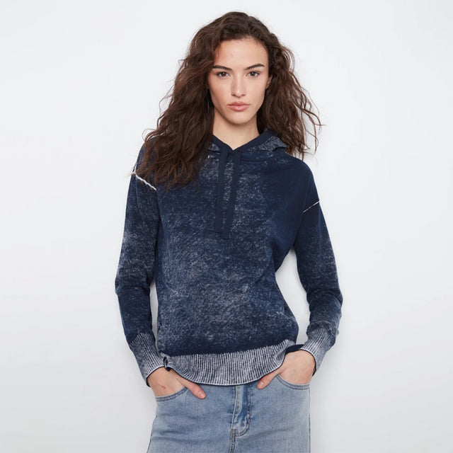 A woman modeling a dark navy blue hooded sweatshirt with a textured, mineral-wash finish and a half-zip neckline, paired with light-wash blue jeans against a plain white studio background.