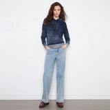 A woman stands against a white wall wearing a dark blue marled knit hoodie with light blue wide-leg jeans and dark brown leather shoes.