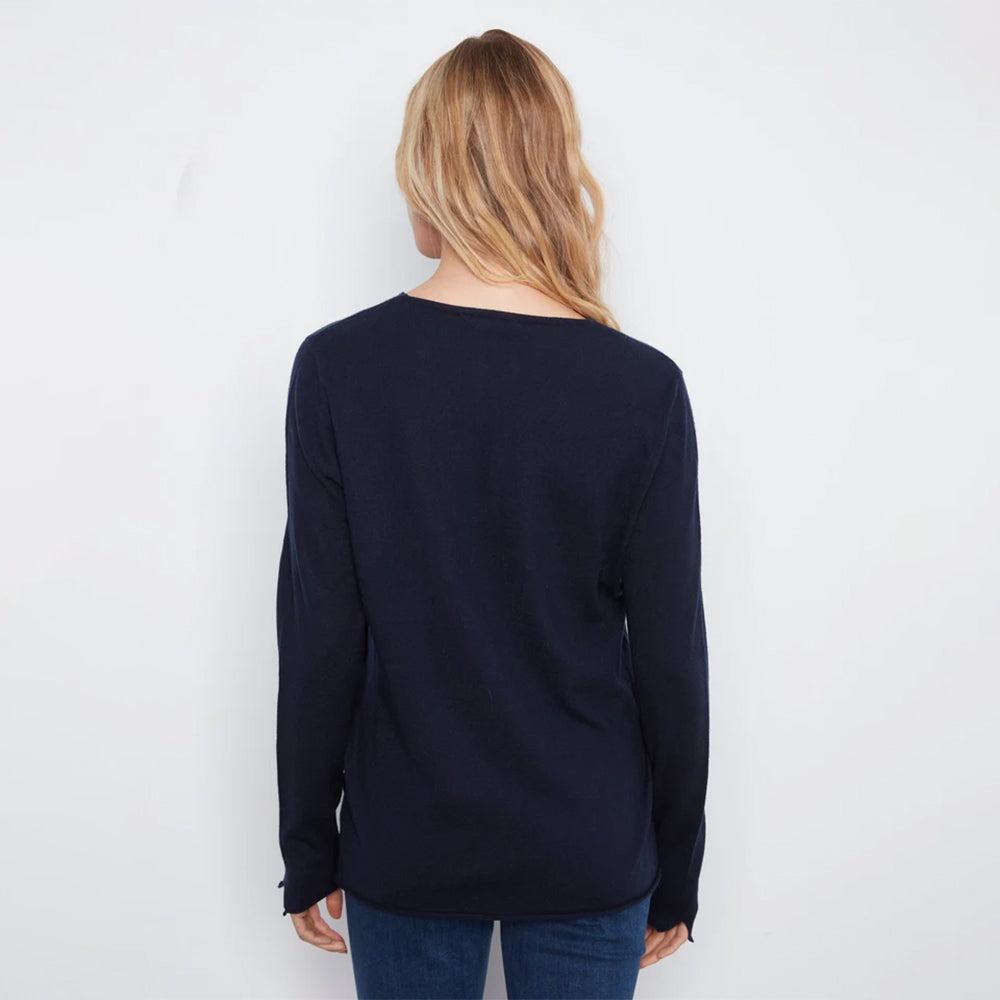 A woman viewed from behind wearing a dark navy long-sleeve knit top and blue jeans against a plain white background.