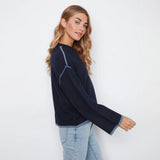 A woman wearing a dark navy blue knit sweater with light blue contrast stitching and light-wash blue jeans, photographed against a plain white studio background.