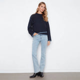 A woman modeling a dark navy blue cropped crewneck sweatshirt with light blue denim jeans and black ankle boots, standing against a plain white wall.
