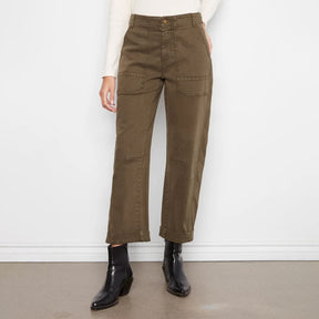 A model wearing olive green wide-leg cropped pants, a cream long-sleeve top, and black ankle boots, standing against a plain white wall.