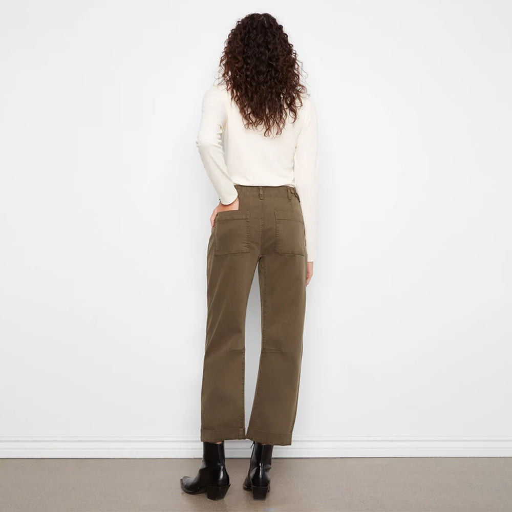 A model viewed from behind wearing olive green wide-leg cropped pants, a cream long-sleeve top, and black ankle boots, standing against a plain white wall.