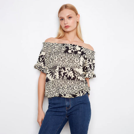 Woman wearing a black and white patterned off-shoulder top with blue jeans on a white background