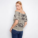 Woman wearing a patterned off-shoulder top and jeans on a white background