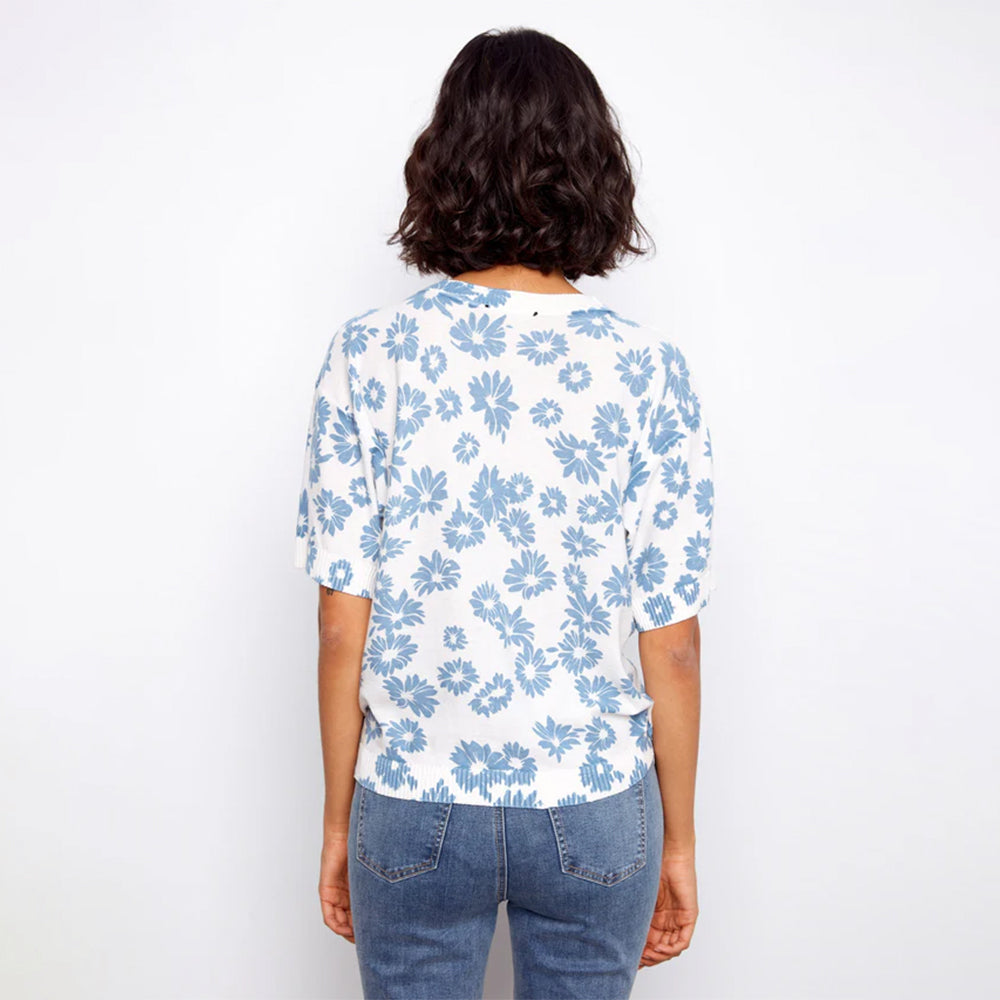 Person wearing a white blouse with blue floral pattern and blue jeans on a white background