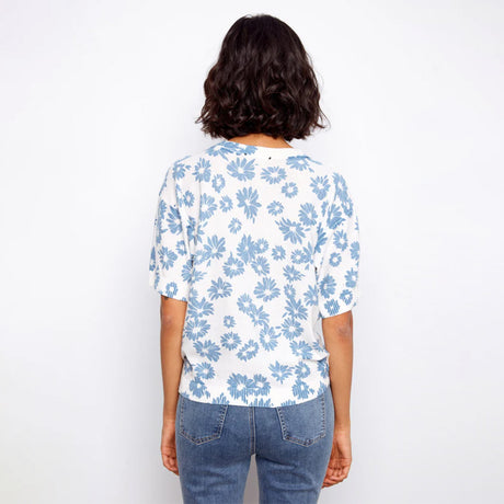 Person wearing a white blouse with blue floral pattern and blue jeans on a white background