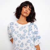 Woman wearing a white t-shirt with blue floral pattern against a plain background