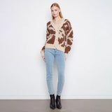 A woman modeling a brown and beige cow-print fuzzy cardigan sweater, paired with light blue skinny jeans and black ankle boots, standing against a plain white wall.