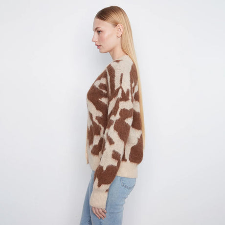 A woman shown in side profile wearing a fuzzy knit sweater with a brown and beige abstract pattern, paired with light blue jeans, against a plain white studio background.