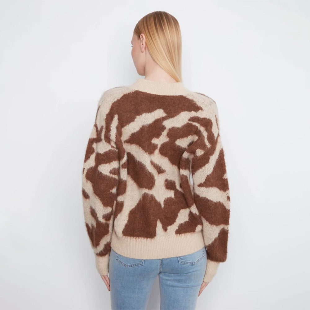 A woman viewed from behind wearing a fuzzy knit sweater with a brown and beige abstract pattern, paired with light blue jeans, against a plain white background.